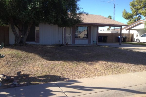 Single-story house with gravel front yard, large tree, carport, and driveway on a sunny day.