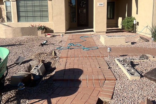 Brick walkway under construction in a front yard with hoses, tools, and building materials scattered around.