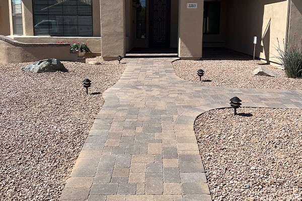 Stone paver walkway leads to a house entrance, bordered by desert landscaping with rocks and minimal plants.