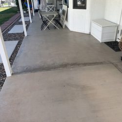 Covered patio with concrete floor, a small table and chairs, white storage box, and coats hanging in the background.
