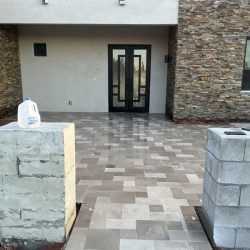 A tiled front entryway with a double glass door, two unfinished block columns, and a gallon water jug on the left column.