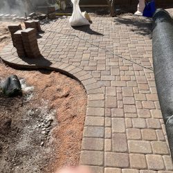 A newly installed brick paver patio with stacked bricks, landscaping materials, and a finger partially covering the lens.