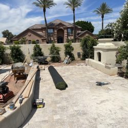 Backyard under construction with paving stones, landscaping tools, a rolled turf, and a built-in outdoor fireplace.