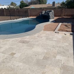 Backyard with a swimming pool, rock feature, and partially completed stone patio next to an unfinished dirt area.