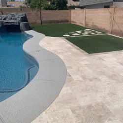 Backyard with a swimming pool, stone patio, and artificial turf area with a large white checkerboard pattern.