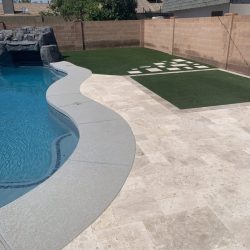 A backyard with a swimming pool, stone patio, artificial turf, and a hopscotch grid painted on the grass.