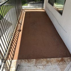 A rectangular patio area with a dirt surface, bordered by black metal railings and adjacent to a house wall.