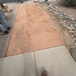 Rectangular area of leveled sand next to a sidewalk, with construction materials and tools visible nearby.